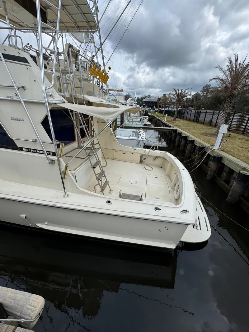 Slide: The Image of 1984 Hatteras 46 Convertible yacht docked, featuring spacious deck and fishing equipment. - 25