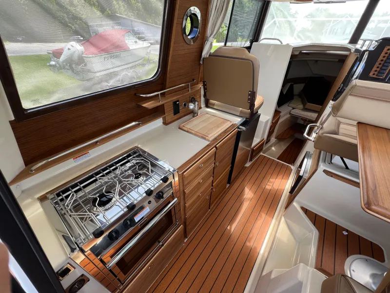 Slide: The Image of 2024 Ranger Tugs R-27 interior with wood finish, featuring a compact kitchen and seating area. - 12