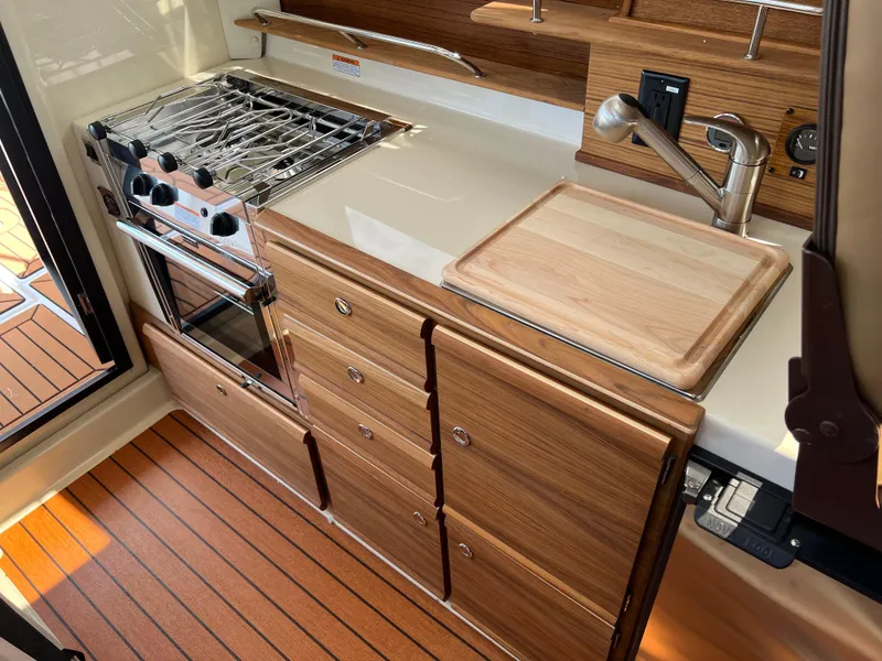 Slide: The Image of 2024 Ranger Tugs R-27 kitchen with stove, wooden cabinetry, and cutting board. - 20