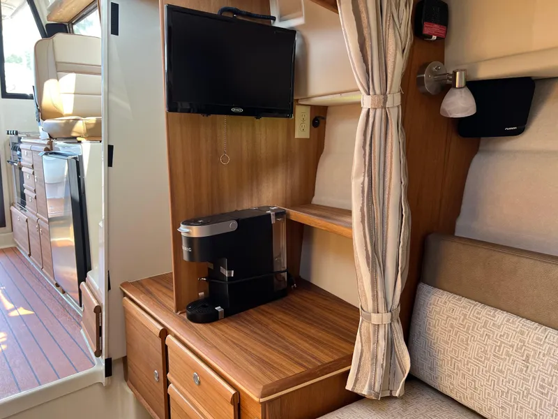 Slide: The Image of 2024 Ranger Tugs R-27 interior with TV, coffee maker, and wooden cabinetry. - 28