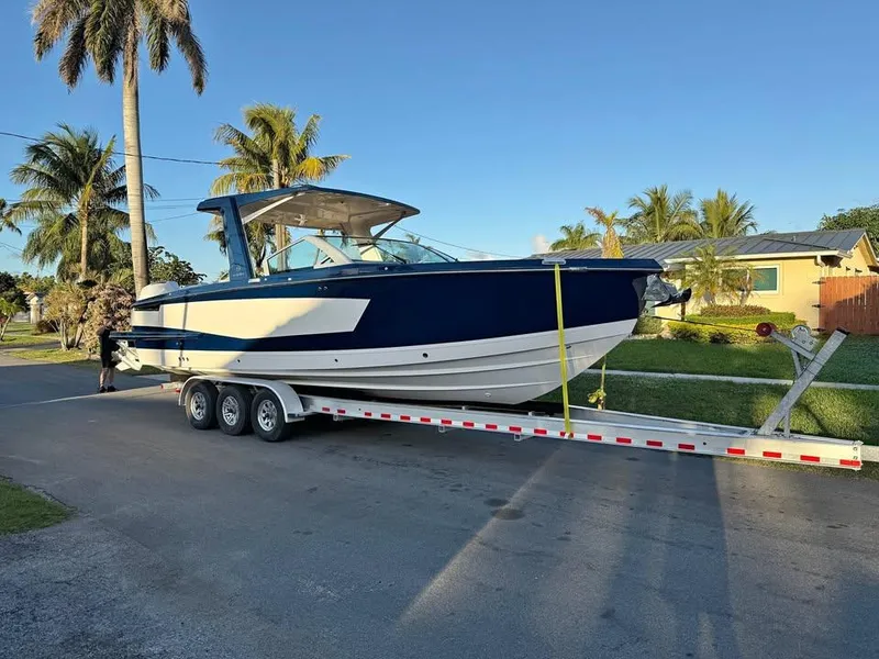 Slide: The Image of 2023 Aviara AV32 OB boat on trailer, parked on a sunny street with palm trees. - 1