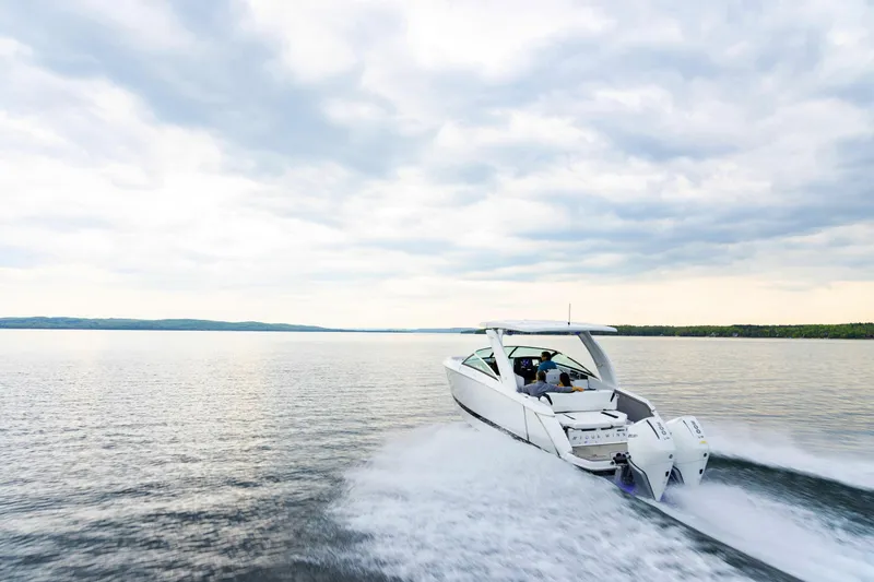 Slide: The Image of 2025 Four Winns H9 OB boat cruising on a serene lake under a cloudy sky. - 2