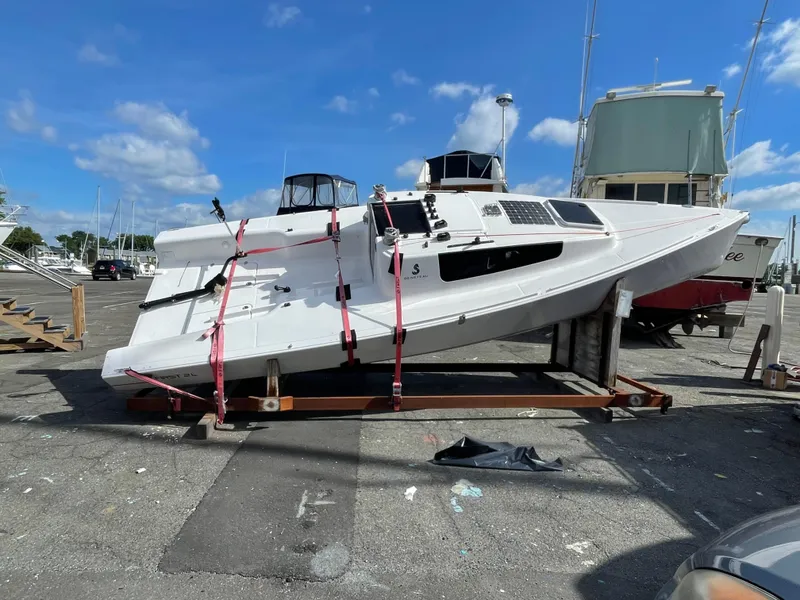 Slide: The Image of 2025 Beneteau First 24 sailboat on a stand, secured with red straps, under a clear sky. - 0