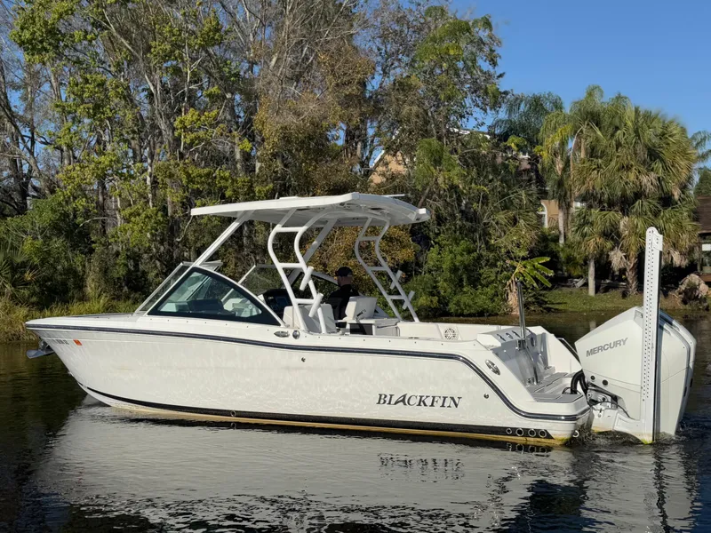 Slide: The Image of 2021 Blackfin 252DC boat on a calm lake with lush greenery in the background. - 29