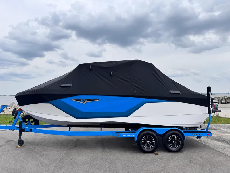 Slide: The Image of 2025 Nautique Super Air Nautique S23 boat covered on trailer, cloudy sky background. - 33