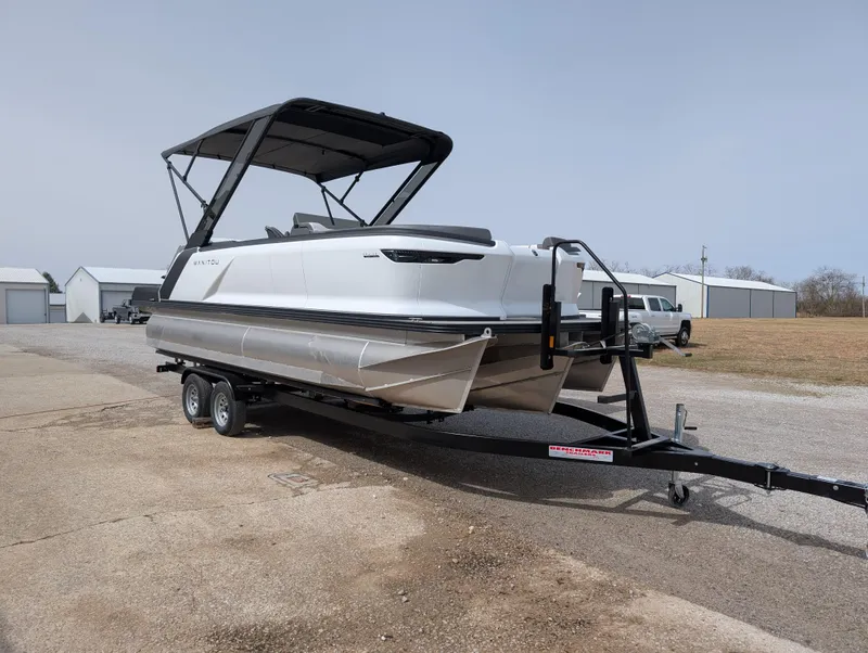 Slide: The Image of 2025 Manitou Cruise pontoon boat on trailer, parked outdoors. - 2