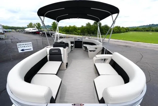 Slide: The Image of 2025 Harris Breeze 210 pontoon boat with spacious seating and canopy, parked near showroom entrance. - 7