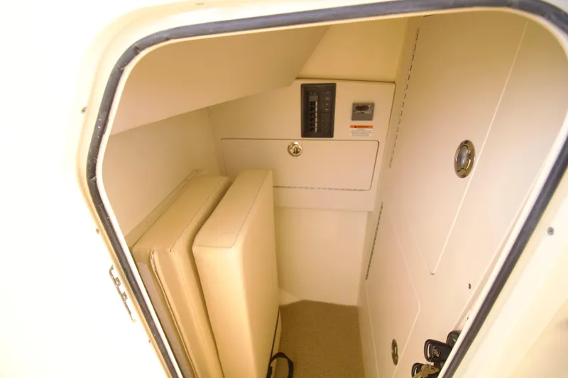 Slide: The Image of 2025 Chris-Craft Calypso 32 interior storage compartment with beige cushions and control panel. - 34