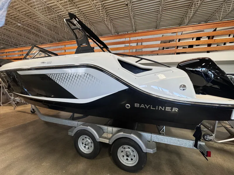 Slide: The Image of 2025 Bayliner D22 boat on trailer in showroom, sleek black and white design. - 0