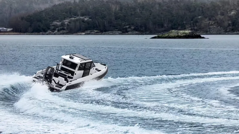 Slide: The Image of A 2025 Iron 827C boat navigating through open water with a forested island in the background. - 2