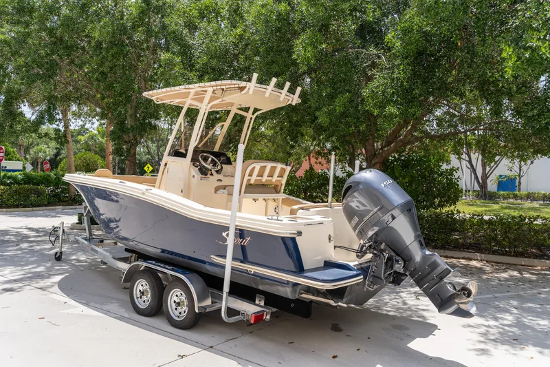 Slide: The Image of 2023 Scout 215 XSF boat on trailer, parked outdoors near trees. - 3