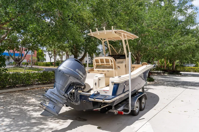 Slide: The Image of 2023 Scout 215 XSF boat on trailer, parked outdoors under trees. - 4