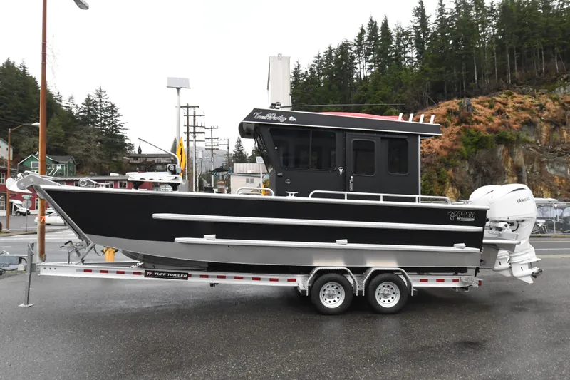The Image of Custom 2025 24 LC boat on trailer, black hull, parked outdoors near forested area. - 0