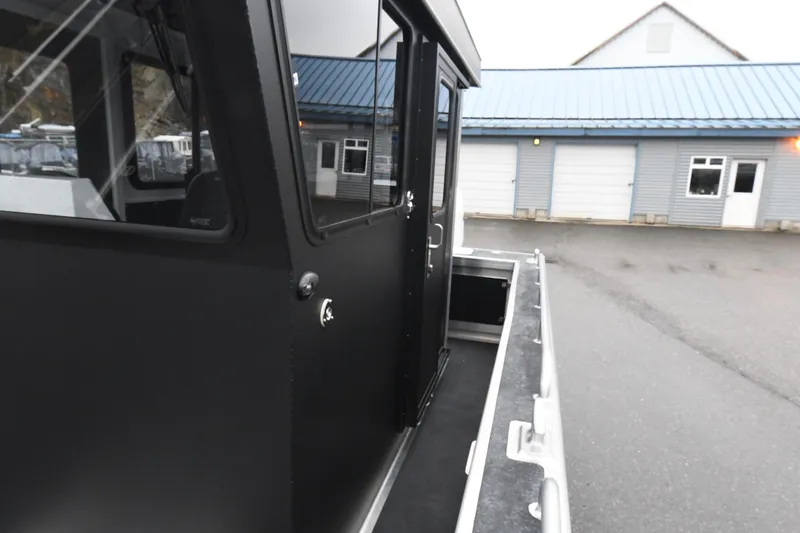 Slide: The Image of Custom 24 LC boat exterior, 2025 model, black cabin, parked near blue-roofed building. - 14