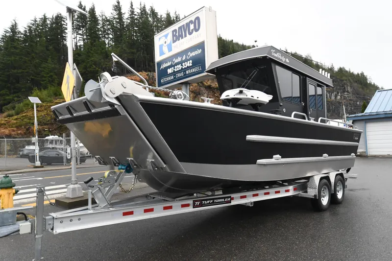 Slide: The Image of Custom 2025 24 LC boat on trailer, parked outdoors near trees and buildings. - 2