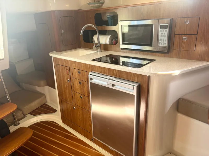 Slide: The Image of 2012 Pursuit OS 345 Offshore boat interior kitchen with wood cabinetry, microwave, and stainless steel appliances. - 12