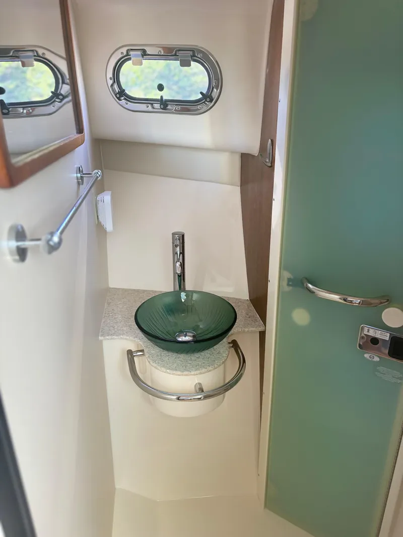 Slide: The Image of 2012 Pursuit OS 345 Offshore bathroom with modern glass sink and porthole window. - 17