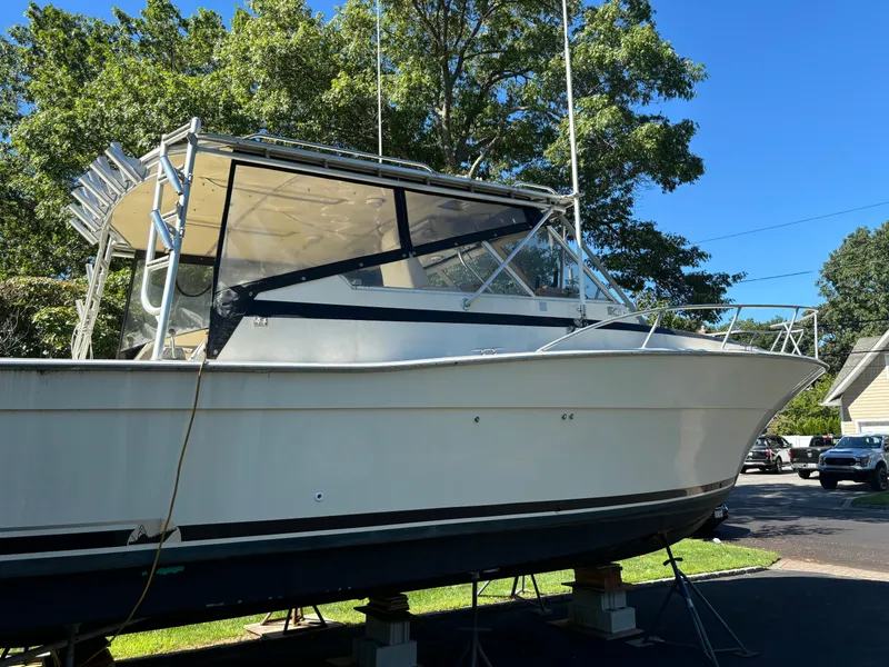 The Image of 1984 Viking Express Cruiser boat on stands, surrounded by trees and clear blue sky. - 1