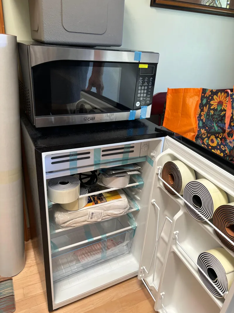 Slide: The Image of Small kitchen setup with a microwave on a mini fridge, storing various items. - 16