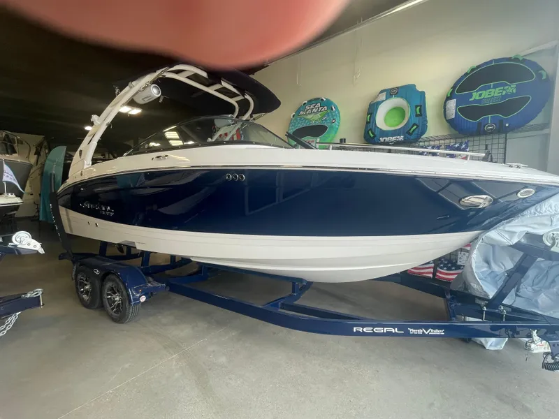 The Image of 2025 Regal LS4 Surf boat in showroom, blue and white design, on trailer. - 0