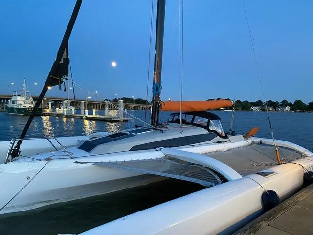 The Image of 2021 Corsair 880 trimaran docked at sunset, with bridge and moon in background. - 1