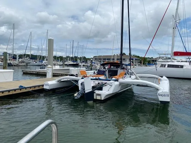 Slide: The Image of 2021 Corsair 880 trimaran docked at marina, surrounded by sailboats under cloudy sky. - 5