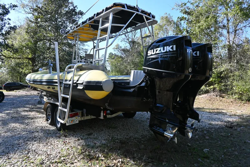 Slide: The Image of 2007 Ribcraft 9.0 boat with Suzuki engines on a trailer, parked outdoors. - 2