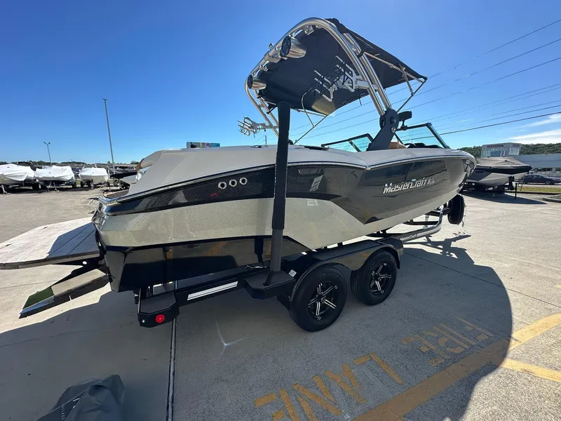 Slide: The Image of 2021 MasterCraft NXT22 boat on trailer, parked outdoors under clear sky. - 2