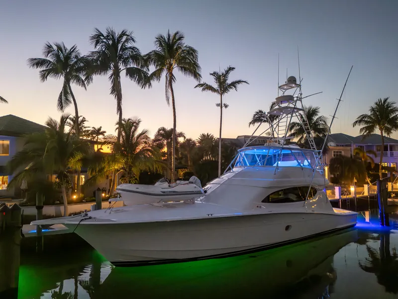 Slide: The Image of 2008 Hatteras 68 Convertible yacht illuminated at sunset, docked near palm trees. - 13