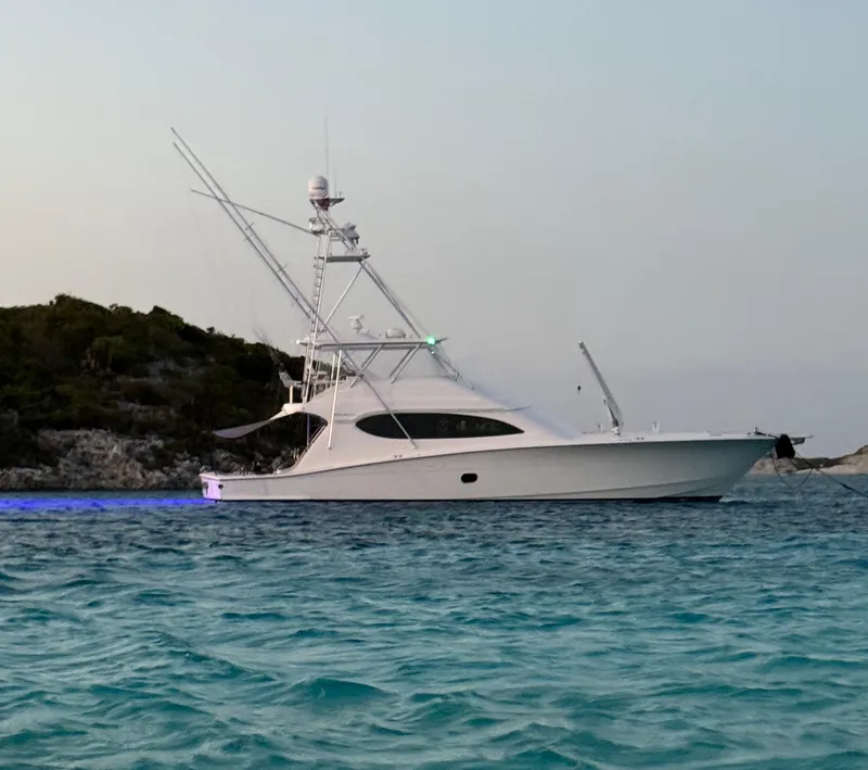 Slide: The Image of 2008 Hatteras 68 Convertible yacht anchored in clear blue waters near a rocky shoreline. - 84