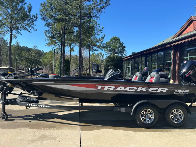 The Image of 2025 Tracker Savage 215 boat on trailer, parked outdoors near trees and building. - 0