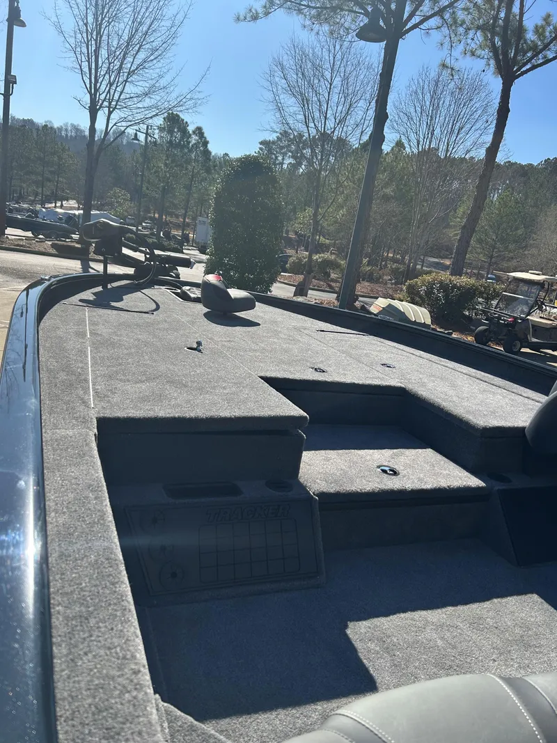 Slide: The Image of 2025 Tracker Savage 215 boat deck with seating, surrounded by trees and clear sky. - 3