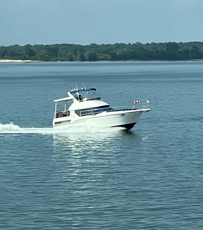 Slide: The Image of 1994 Carver 350 Aft Cabin cruising on a serene lake with forested shoreline. - 2