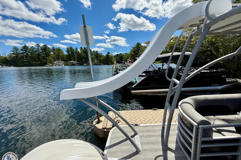 Slide: The Image of 2025 Bennington 26 LSRTD pontoon boat with slide, docked on a sunny lake. - 16