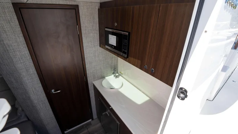 Slide: The Image of Interior of 2025 Everglades 455 CC boat featuring kitchenette with wood cabinets and microwave. - 24
