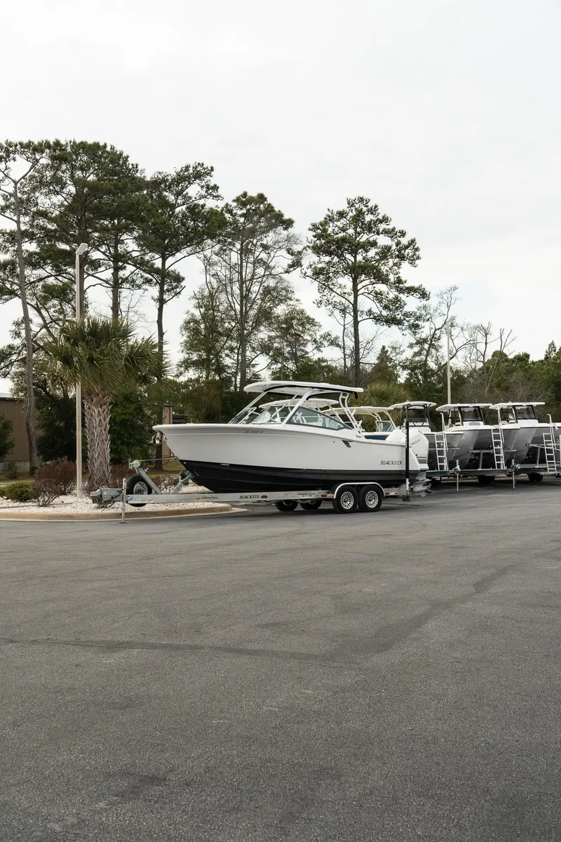 Slide: The Image of 2023 Blackfin 272 DC boat on trailer in parking lot, surrounded by trees. - 30