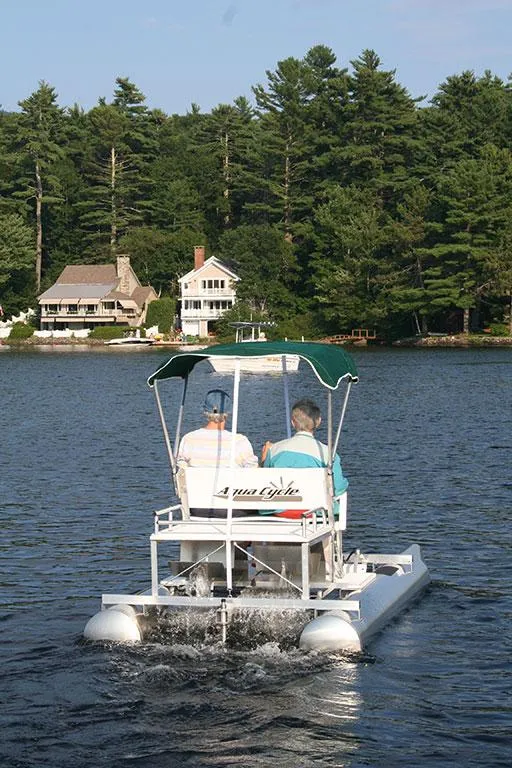 Slide: The Image of 2024 Aqua Cycle AC15W pedal boat on a serene lake with forested shoreline. - 2