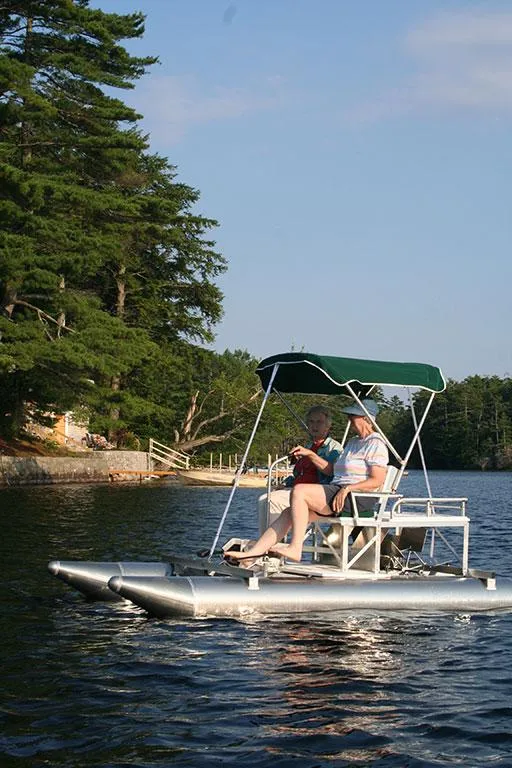 Slide: The Image of 2024 Aqua Cycle AC15W pontoon boat on a serene lake with two passengers. - 5