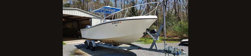 The Image of 1990 Mako 261 Center Console boat on trailer, parked outdoors near a garage. - 0
