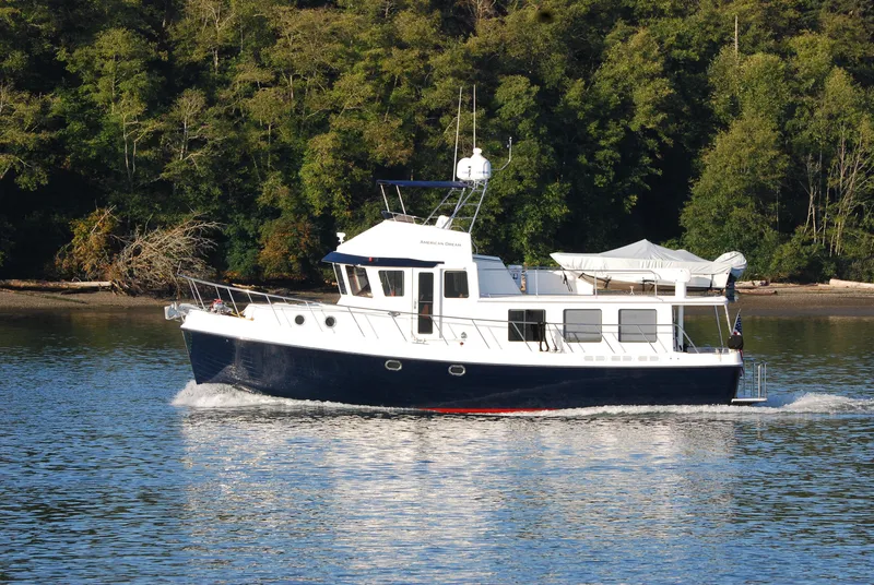 Slide: The Image of 2015 American Tug 485 cruising on a calm river with lush forest backdrop. - 2
