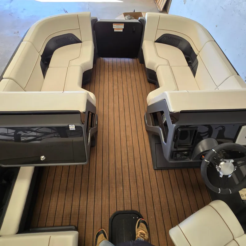 Slide: The Image of 2024 Manitou Explore 22+4 Switchback boat interior with spacious seating and wood-style flooring. - 12