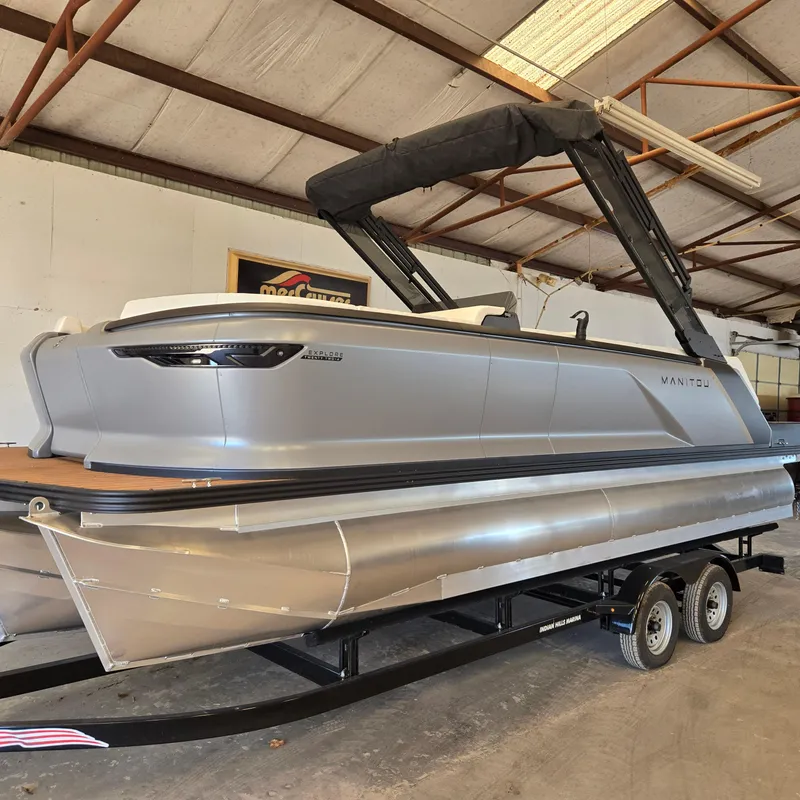 Slide: The Image of 2024 Manitou Explore 22+4 Switchback pontoon boat on trailer in warehouse. - 3