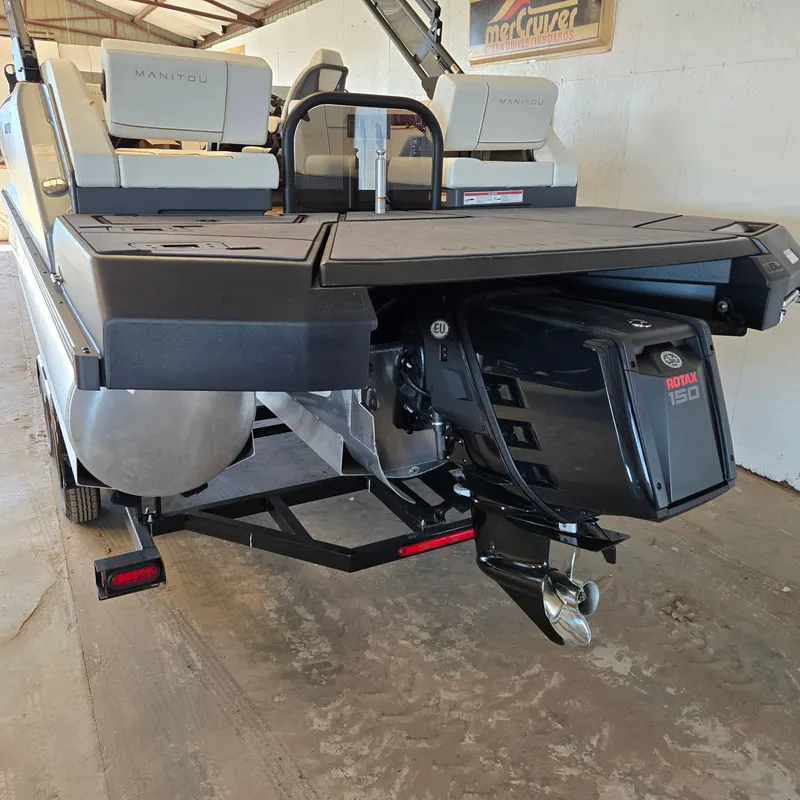 Slide: The Image of 2024 Manitou Explore 22+4 Switchback boat with powerful motor, rear view in a garage. - 4