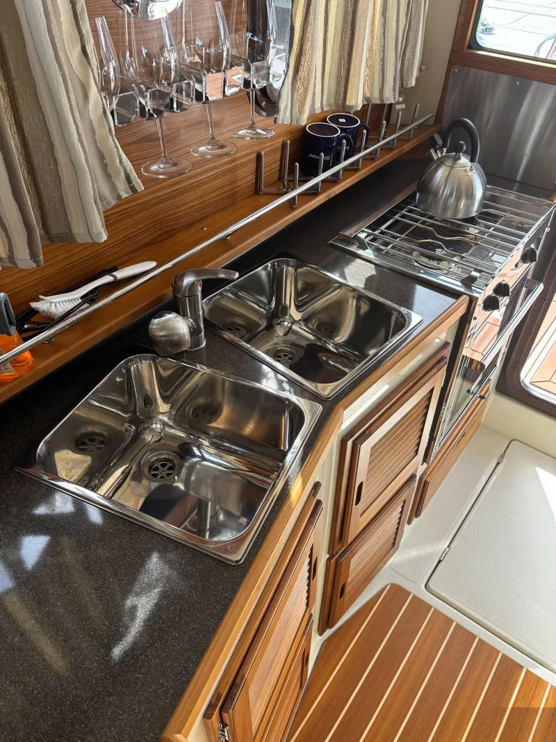 Slide: The Image of 2024 Ranger Tugs R31S kitchen with dual sinks, stove, and wooden cabinetry. - 10