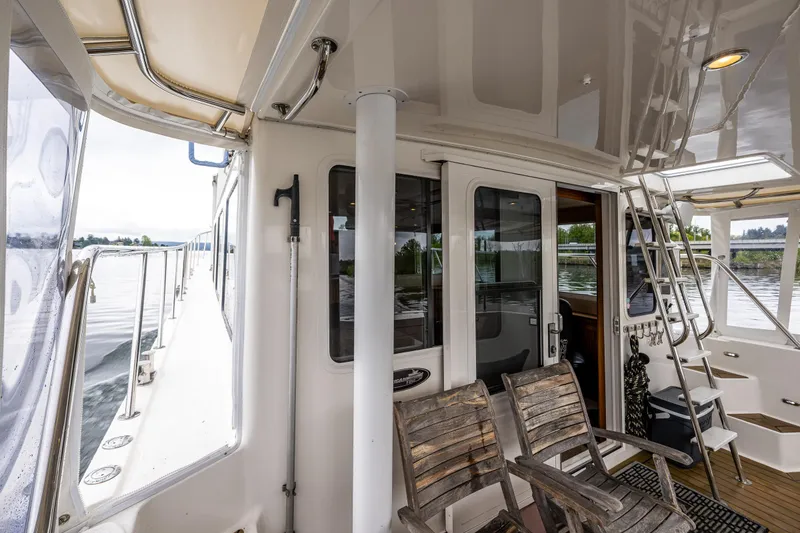 Slide: The Image of 2009 American Tug 49 Limited yacht deck with wooden chairs and scenic water view. - 35