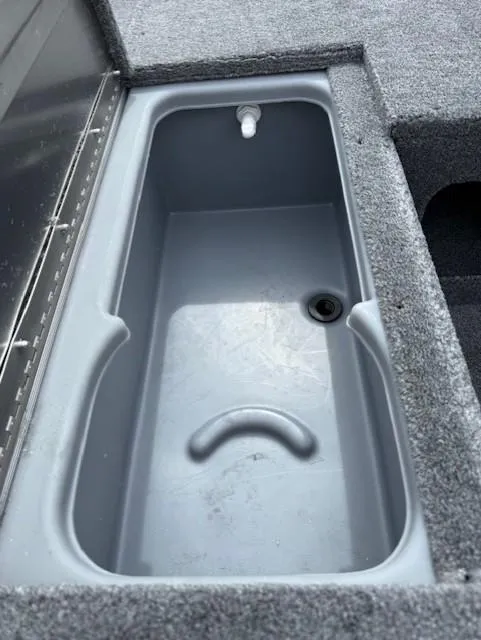Slide: The Image of 2025 Tracker Pro 170 boat storage compartment with gray interior and drain plug. - 6