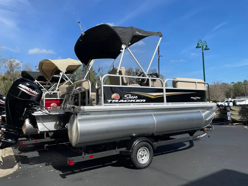 Slide: The Image of 2025 Sun Tracker Party Barge 16 DLX pontoon boat on trailer, parked outdoors. - 2