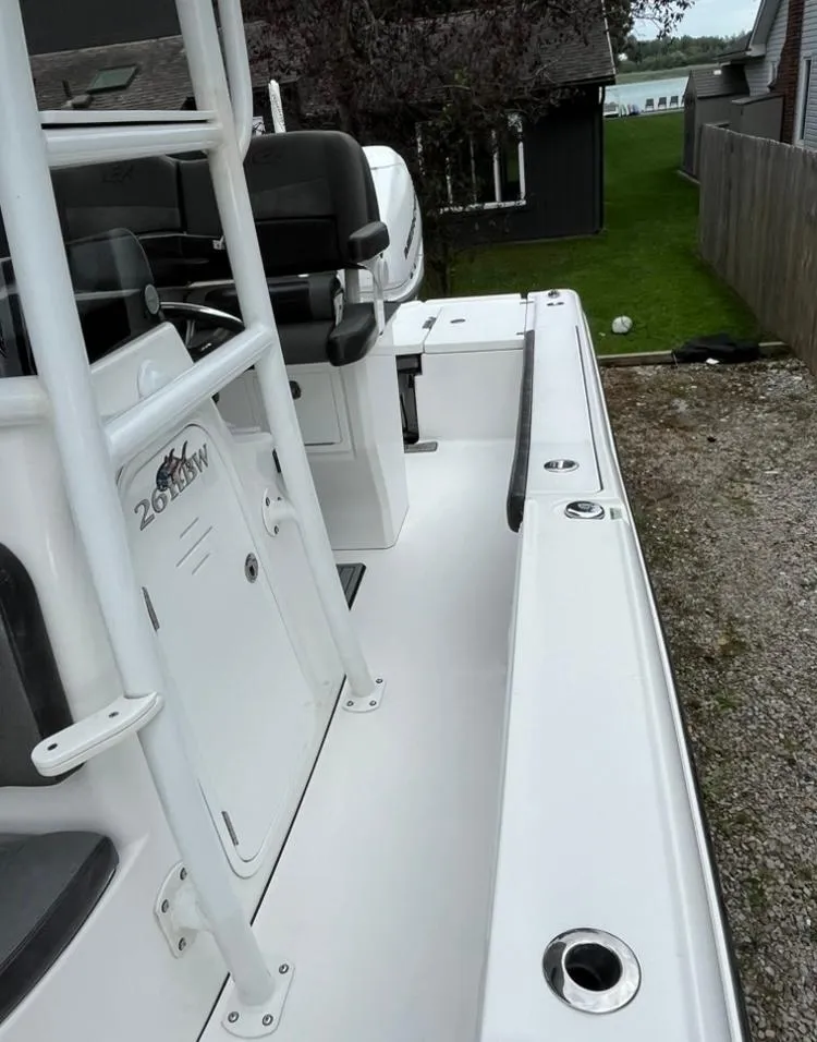 Slide: The Image of 2020 Crevalle 26 HBW boat, white deck, rod holders, and seating, parked near a house. - 16