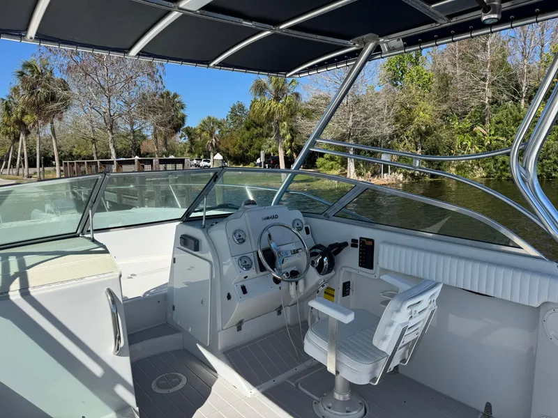 Slide: The Image of 2004 Glacier Bay Renegade 2640 boat cockpit with steering wheel and seating, surrounded by lush greenery. - 30