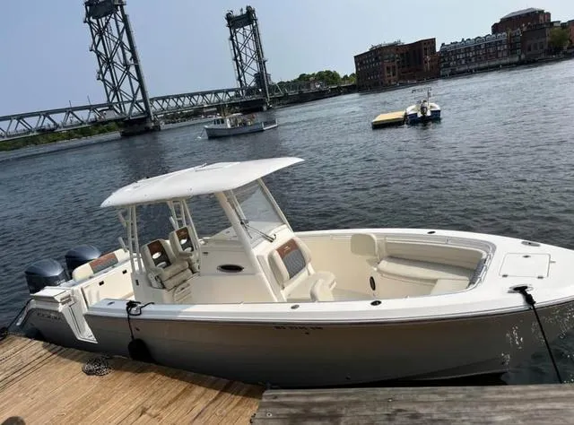 Slide: The Image of 2019 Cobia 301CC boat docked by a river with a bridge in the background. - 1